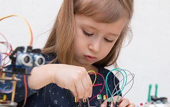 A girl constructs metal robot and program it. The boards and micro controllers are on the table.