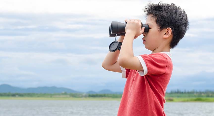 Boy in a field looking through binoculars
