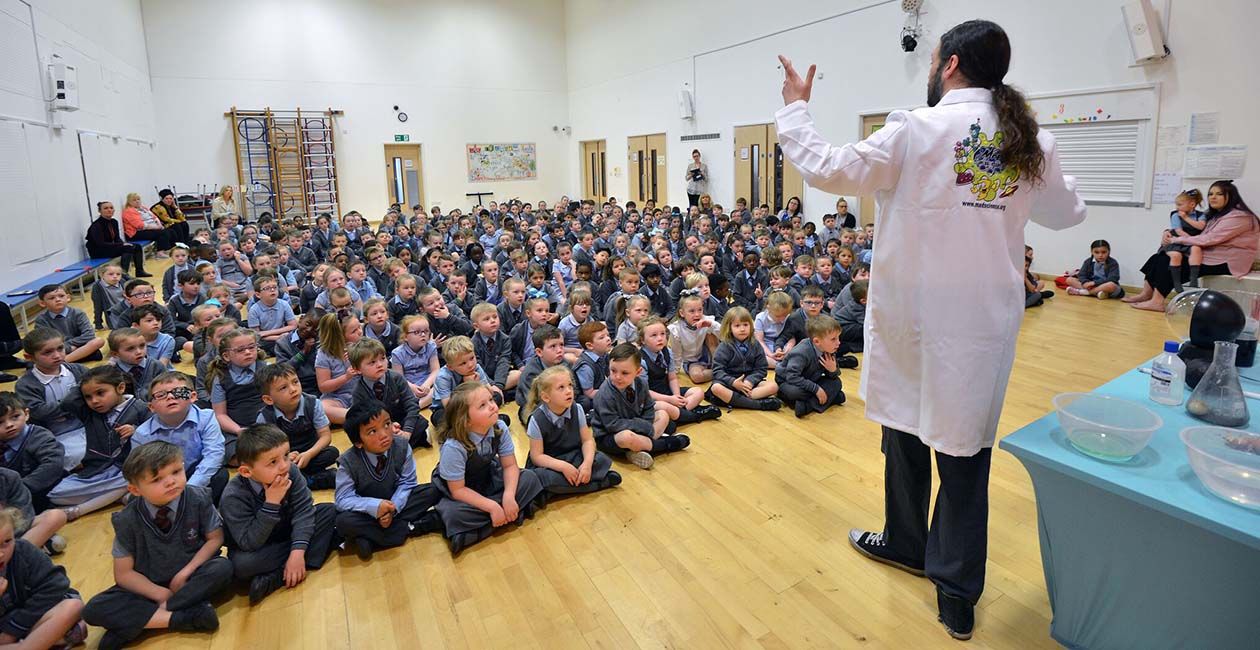 Young students sitting on the gym floor watching a Mad Science special event