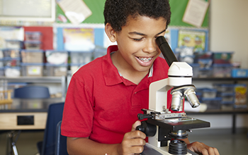 Boy in red shirt looking though a microscope in a classroom